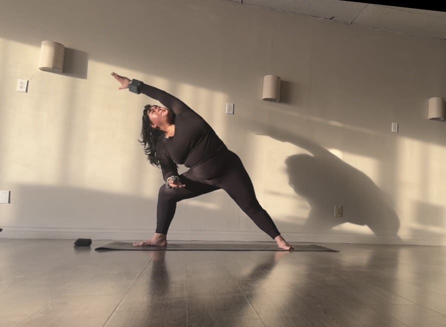 Liberty Apolinario stands in a yoga pose wearing a black athletic outfit in a brightly lit studio
